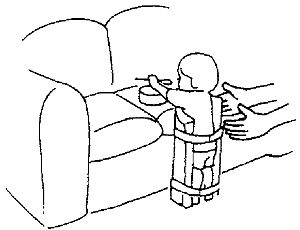 Ребенок с умеренными нарушениями мышечного тонуса играет, стоя у дивана
